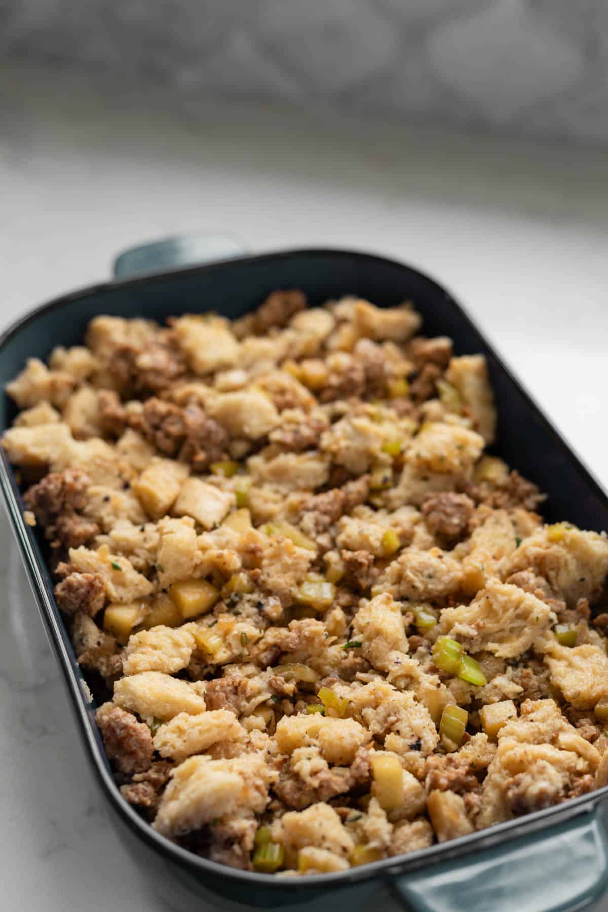 uncooked sausage and apple stuffing in a blue pan on a white counter