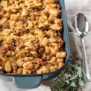 sausage and apple stuffing in a blue pan with herbs next to it and a silver spoon