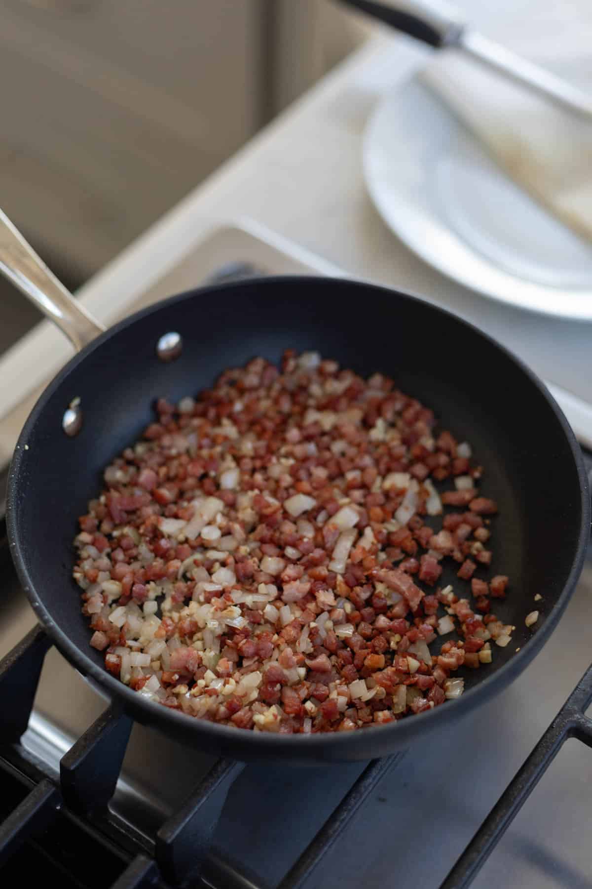 pancetta, garlic, and shallots being cooked in a small black skillet