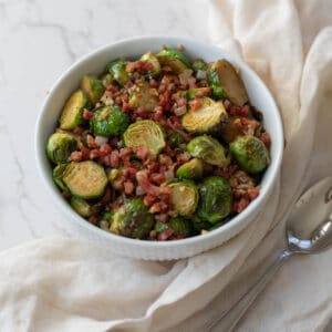 roasted brussels sprouts with diced pancetta in a white bowl on a white napkin