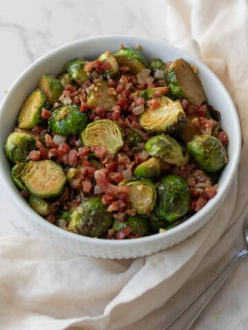 roasted brussels sprouts with diced pancetta in a white bowl on a white napkin