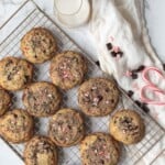 peppermint chocolate cookies on a wire baking rack next to a glass of milk, candy canes, and chocolate chunks