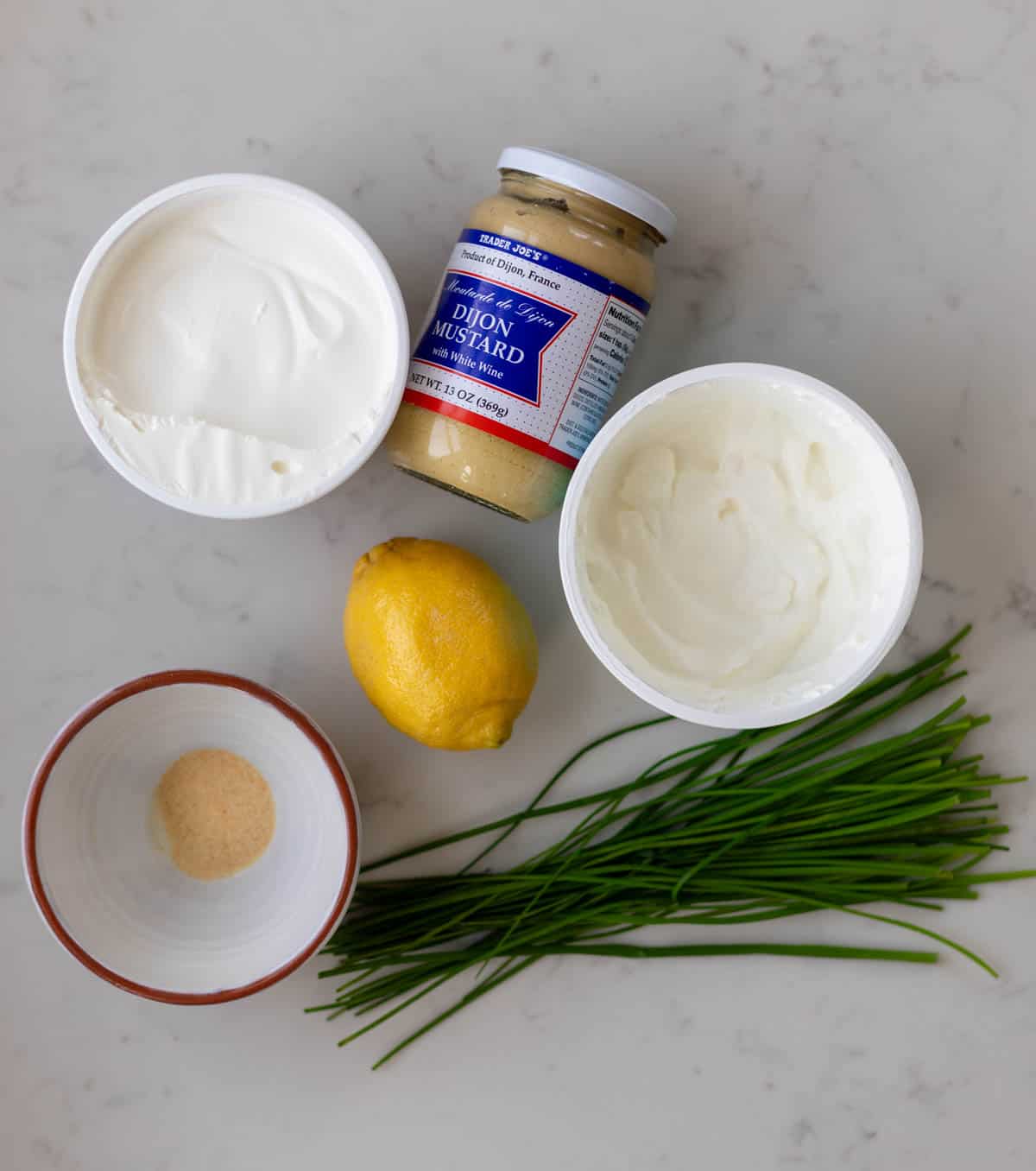 sour cream, greek yogurt, dijon, a lemon, chives and garlic powder on a white counter