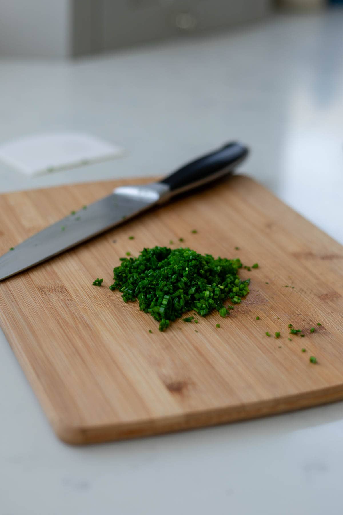 chopped chives on a wooden cutting board next to a knife
