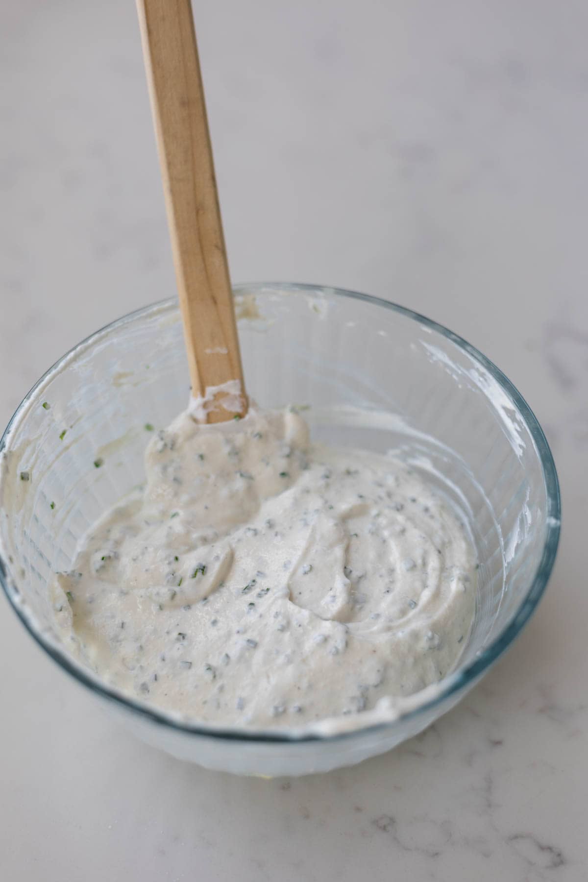 sour cream and chive dip in a glass bowl with a wooden spatula sticking out