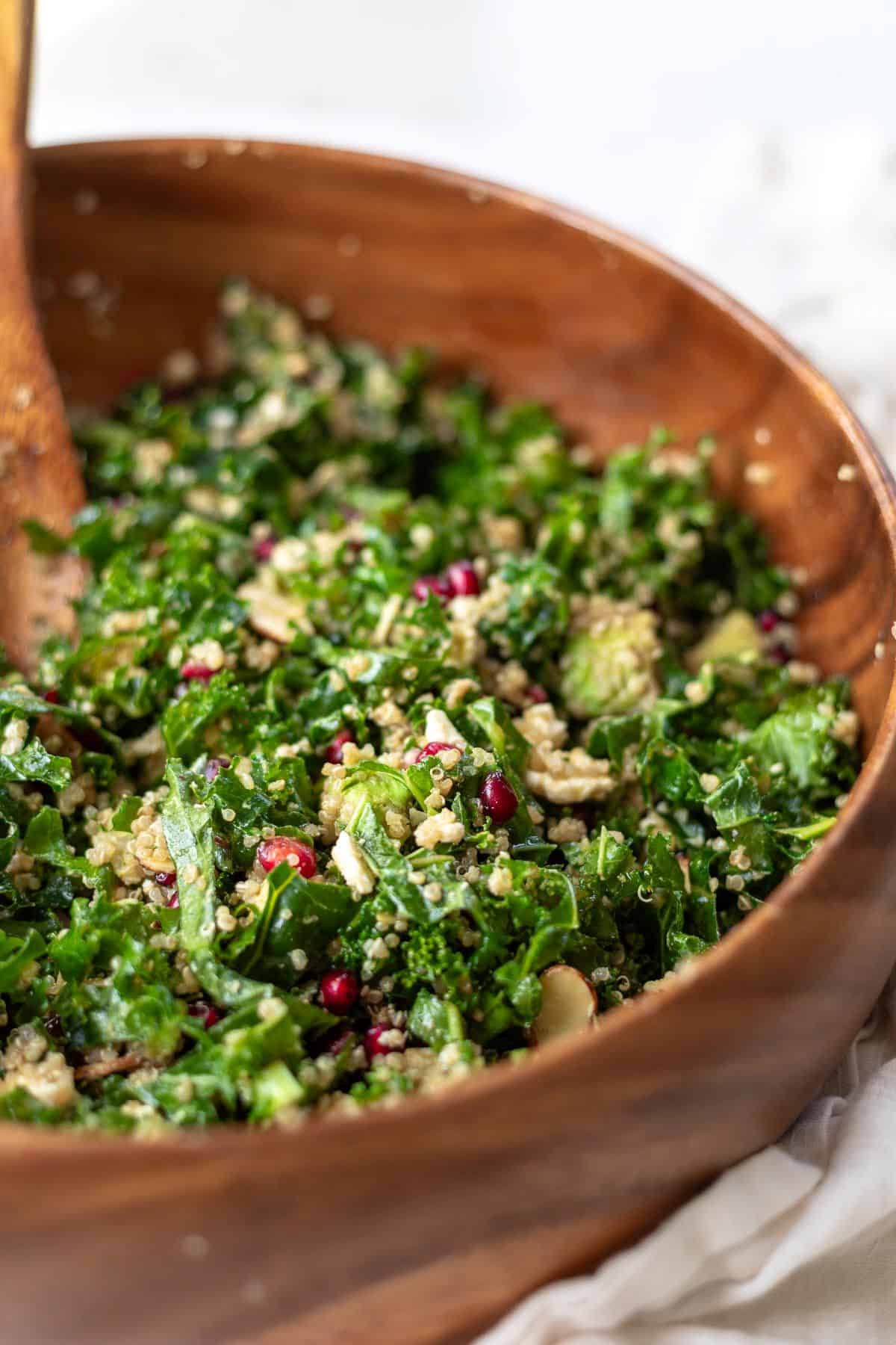 Tossed kale salad with pomegranates and quinoa in a wood bowl.