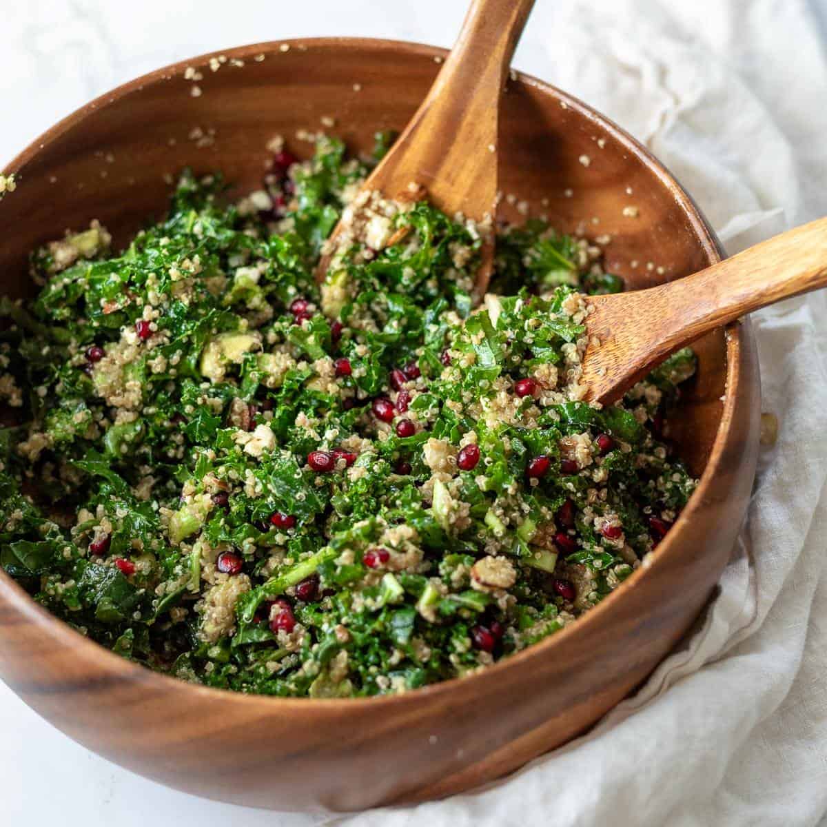 Tossed kale salad with pomegranates and quinoa in a wood bowl.