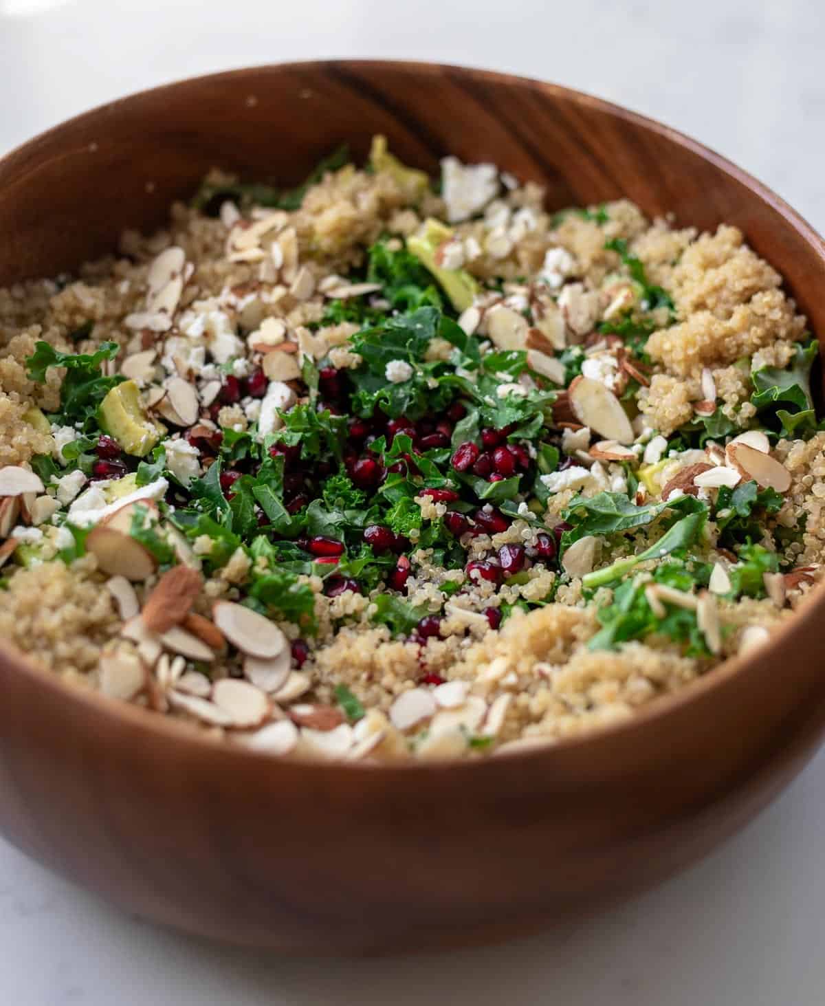 Kale, pomegranates, quinoa, almonds, and feta in a wood salad bowl.