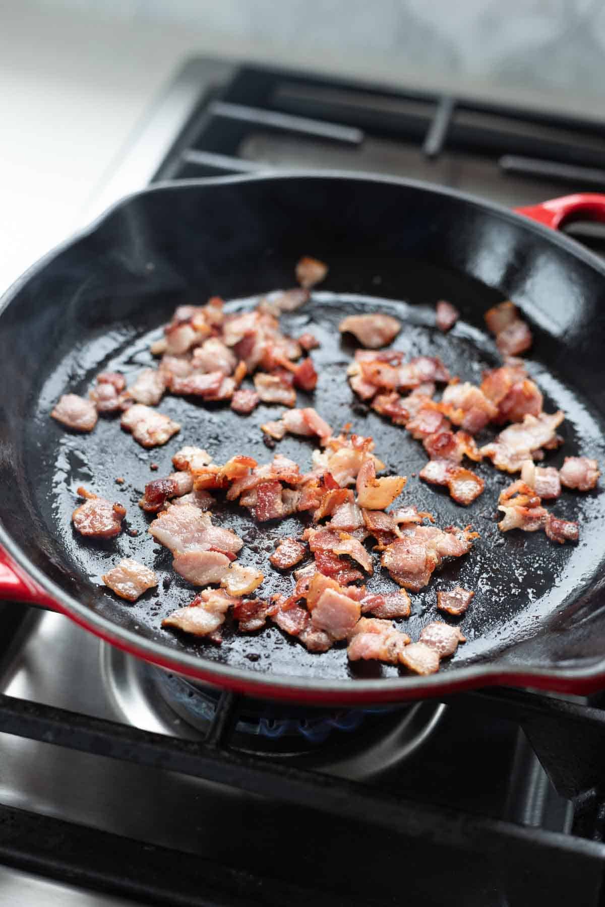 Bacon bits cooking in a cast iron skillet.