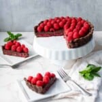 Chocolate raspberry tart on a pie dish next to two slices of tart, mint, and forks.