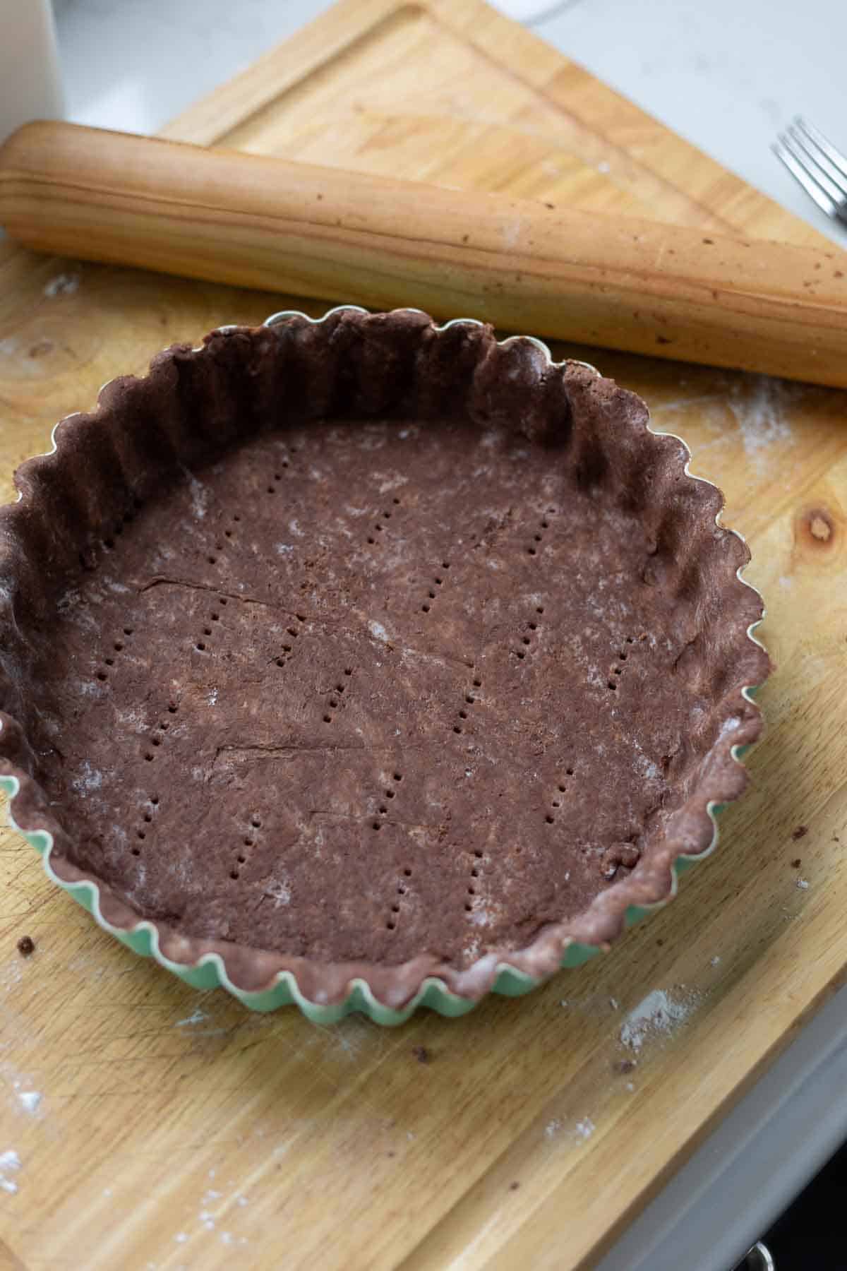 Chocolate tart crust in a tart pan on a cutting board.