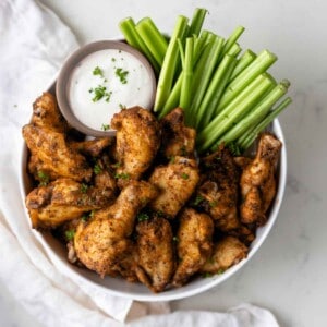 Dry rub chicken wings in a bowl next to celery sticks and ranch dressing.