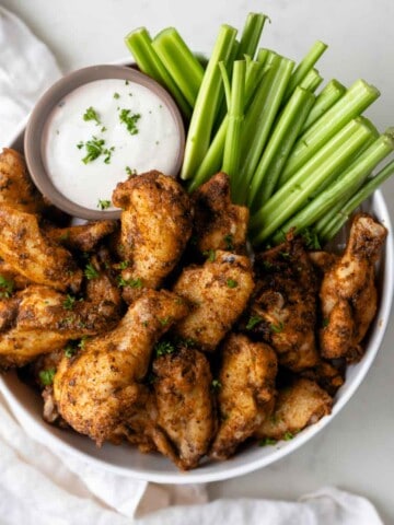 Dry rub chicken wings in a bowl next to celery sticks and ranch dressing.