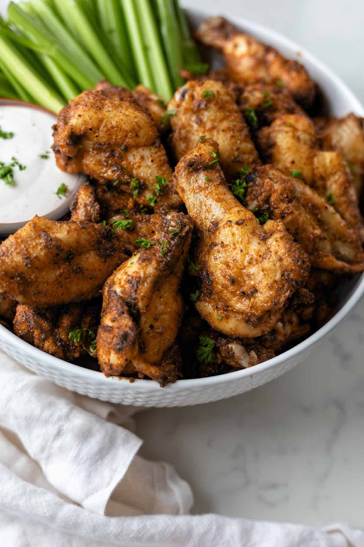 Close up photo of dry rub chicken wings in a bowl next to celery sticks and ranch.