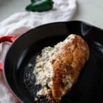 Cooked jalapeno popper and bacon stuffed chicken breast in a cast iron skillet.