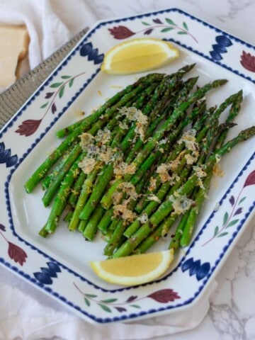 Roasted asparagus on a platter with lemon wedges and a block of parmesan next to it.