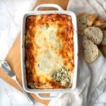 Baked hot spinach and artichoke dip made without mayo in a baking dish on a wooden board next to bread.
