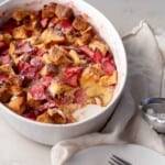Easy strawberry brioche bread pudding in a white baking dish with a portion missing next to powdered sugar.