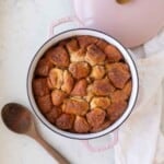 Golden brown monkey bread in a pink Dutch oven next to a wooden spoon.
