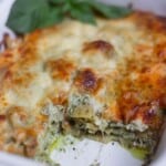 Baked chicken pesto lasagna in a white baking dish with a slice missing revealing the layered pasta, pesto, and chicken.