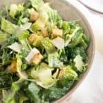 Tossed homemade Caesar salad with croutons, parmesan, and dressing in a grey bowl.