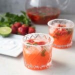 Two glasses of Strawberry Basil Margaritas next to a plate of salt, lime wedge, strawberries, basil, and a pitcher.