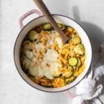 A wooden spoon scooping into a one pot baked zucchini pasta with corn and mozzarella.