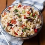 Greek Chicken Pasta Salad in a glass bowl on top of a blue and white towel and wooden table.