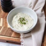 Horseradish Mustard Sauce in a white bowl with a tan napkin and cutting board under it next to a pepper grinder.