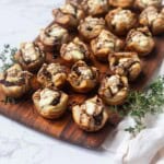 Puff pastry caramelized onion goat cheese bites topped with balsamic glaze on a wooden cutting board next to fresh thyme.